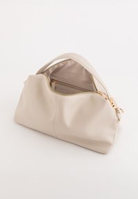 Beżowa skórzana torebka o gładkiej teksturze, zaokrąglonym kształcie i złotych akcentach. W pełni zapinane zapięcie odsłania wewnętrzną kieszeń.