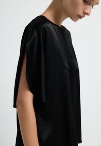 Top in satin nero con vestibilità comoda, maniche corte e scollatura rotonda. Presenta una texture semplice e liscia e dettagli di design minimi.