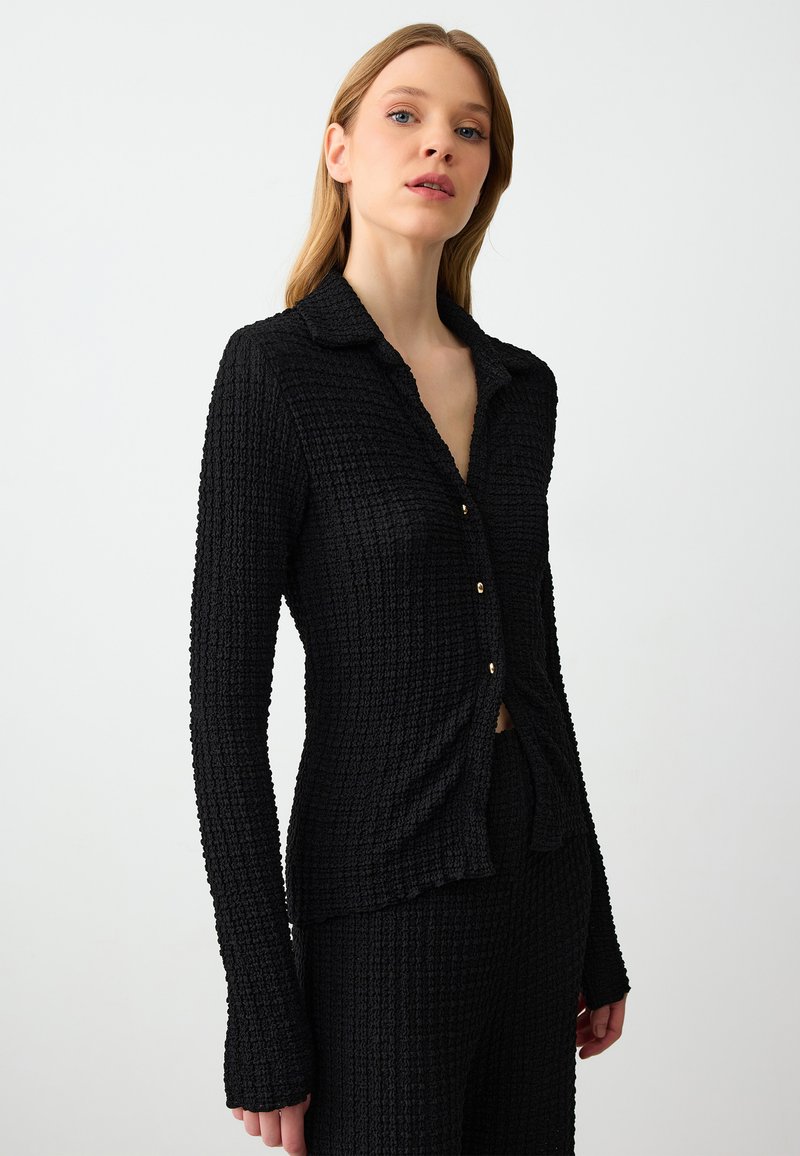 Zwarte button-up shirt van een gestructureerde stof, met lange mouwen en een kraag. Voorzien van kleine gouden knopen en een getailleerd ontwerp.