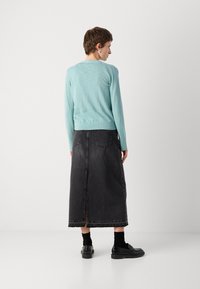 Light blue long-sleeve sweater made of soft fabric, paired with a dark gray denim skirt featuring a back slit and two back pockets. Black shoes and socks.