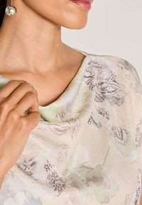 Lichtgewicht, patroon top in zachte stof met een gedrapeerde halslijn. Kleuren omvatten crème, groen en subtiele bloemmotieven.