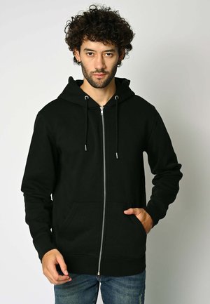 Felpa nera con zip realizzata in tessuto morbido, con tasca frontale, cappuccio regolabile con lacci e polsini a coste. Indossata con jeans blu casual.