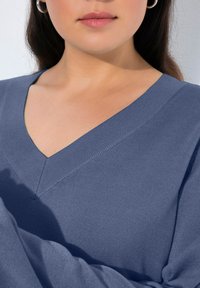 V-Ausschnitt-Pullover aus weichem, geripptem Stoff mit strukturierter Oberfläche, in einem gedämpften Blauton. Mit lockerer Passform und langen Ärmeln.
