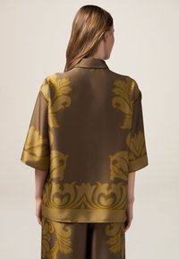 Chemise en satin marron avec des manches surdimensionnées et un motif floral doré, dotée d'un col élégant et d'une texture lisse.