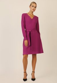 Fuchsia gestricktes Kleid mit langen Ärmeln, V-Ausschnitt und gebundenem Gürtel in der Taille. A-Linien-Silhouette mit glatter Textur.