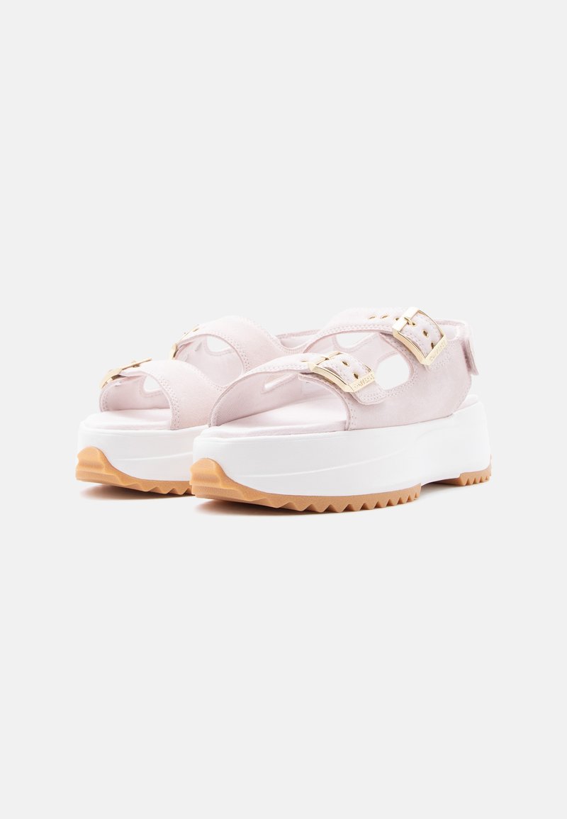 Sandali platform rosa chiaro con suole spesse bianche, fibbie dorate e suole esterne in gomma texturizzata marrone chiaro, mostrati di profilo e frontalmente.