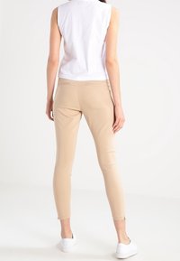 Beiga slim-fit byxor med en slät textur, med anklaresor och en midjehöjd som är varken för hög eller för låg, i kombination med en vit ärmlös topp.