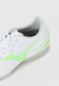 Zapatilla deportiva blanca con superficie texturizada, acentos verdes y un interior gris. El nombre del modelo "MONARCIDA NEO" se muestra en el lateral.