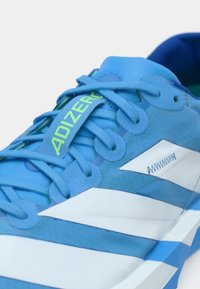 Nahaufnahme eines blau-weißen Laufschuhs mit blauen Schnürsenkeln und der Aufschrift "ADIZERO" in Neon-Gelb auf der Zunge.