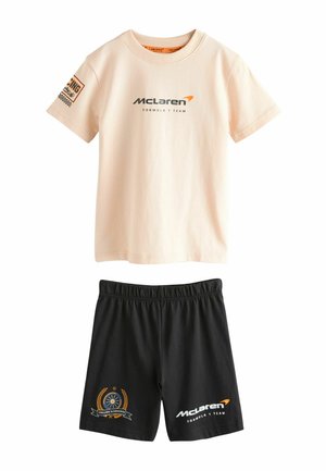 Beżowa koszulka z krótkim rękawem zespołu McLaren Formula 1 oraz czarne szorty z logo i łatkami o tematyce wyścigowej.