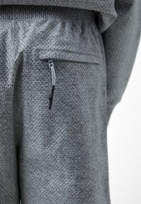 Gray textured trousers featuring a zippered pocket, elastic waistband, and breathable fabric with a perforated pattern.