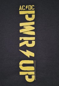 Černé pozadí se svislým žlutým textem "AC/DC POWER UP," přičemž symboly blesku nahrazují lomítka.