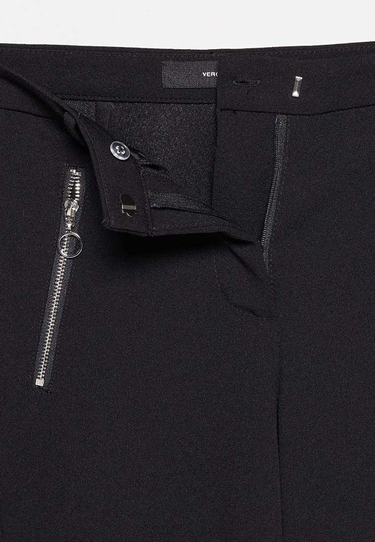 Pantalons noirs ajustés avec une texture douce. Dotés d'une fermeture éclair, d'un bouton et d'un accent en métal rectangulaire. Étiquette visible à l'intérieur.