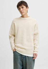 Cremefarvet sweater med ribbet halsudskæring, drop-skulder og en blød tekstur. Parret med løse denimjeans i en bleg blå nuance.
