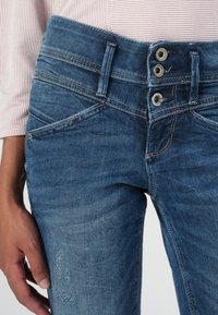 Blå denimjeans har en høy midje med en lukking med tre knapper, fem lommer og en falmet finish med subtile slitasjer på låret.