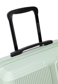Light green hardshell suitcase with vertical ribbed pattern, featuring a black telescopic handle and zipper closure. Brand logo visible.