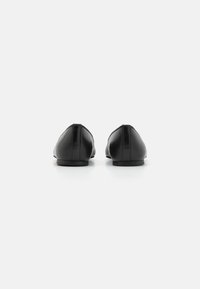 Svarta läderskor med spetsig tå och minimalistisk design, som har en platt klack och slät yta, sedd bakifrån.