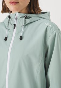 Lys grøn, zip-up jakke med hette, justerbare snorer og sorte stoppere. Har hvit glidelås og CMP-logo på skulderen.