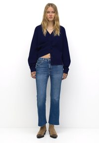 Námořnický modrý pletený cardigan s výstřihem do V, předním zapínáním na knoflíky a balónovými rukávy, doplněný o světle modré zvonové džíny a hnědé kotníkové boty.