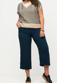 Beige kortärmad tröja med zigzag-mönster; kombinerad med marinblå vida byxor; strukturerad tyg; avslappnade svarta snörskor med halmsulor.