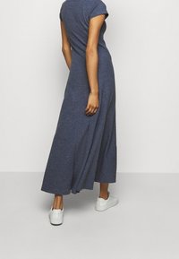 Robepanneau maxi bleu marine à manches courtes avec une coupe décontractée, fabriquée en tissu doux, dotée d'un ourlet fluide et portée avec des baskets blanches.