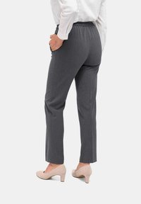 Grijze, op maat gemaakte broek met een elastische tailleband, slim fit en zijzakken. Draagt met lichtgekleurde hakken. Zacht, gevarieerd stof.