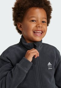 Giacca in pile grigia con colletto alto, zip frontale e loghi bianchi di Adidas e Disney. Texture morbida e polsini aderenti, che offrono comfort e calore.