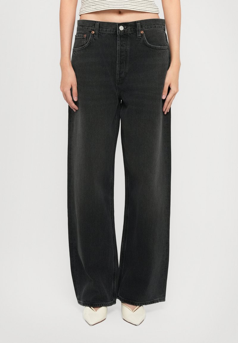 Jean denim noir à jambes larges et taille haute, avec ferrures en cuivre, cinq poches et coutures contrastantes. Texture lisse avec un léger éclat.