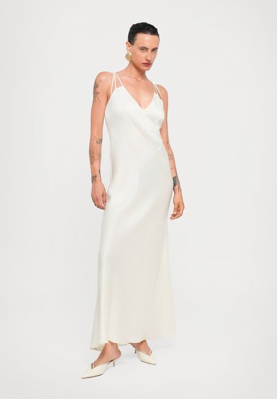 Robe maxi en satin blanc avec un décolleté en V et des bretelles fines. Elle présente un bodice ajusté et une jupe fluide. Associée à des talons slingback crème.