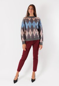 Maglione grigio con motivo a diamante blu, rosa e bordeaux, abbinato a pantaloni slim bordeaux e décolleté nere a punta.