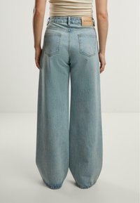 Jeans albastre deschise, cu picioare largi și talie înaltă, având o eticheta din piele bej pe spate și două buzunare pe spate. Textură moale de denimul.