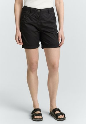 Shorts en coton noir avec fermeture à bouton, poches et ourlets roulés. Assortis avec des sandales noires à double bride et boucles.