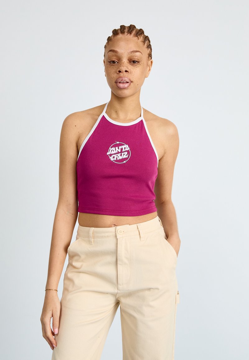 Fialový haltere crop top s bielym lemovaním a logom potlačeným v strede; spárovaný so svetlo béžovými vysokými nohavicami. Hladká bavlnená tkanina.