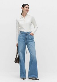 Vahva vaalean beige ribattu pitkähihainen pusero napitettavalla kauluksella yhdistettynä korkeavyötäröisiin, leveälahkeisiin vaaleansinisiin farkkuihin.