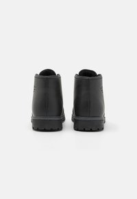 Botas de tobillo de cuero negro con textura suave, punta redonda y suela de goma resistente. Incluye un collar acolchado y una marca en relieve en el talón.