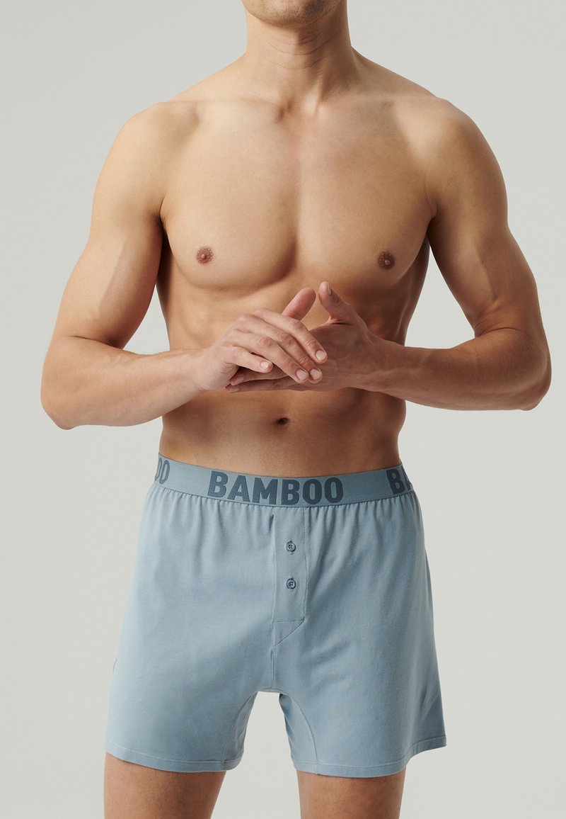 Jasnoniebieskie bokserki z bambusa z ciemnoniebieskim paskiem "BAMBOO", posiadające dwa zapięcia na guziki oraz miękką, gładką teksturę.