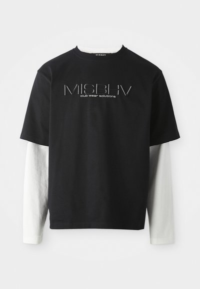 Must have lühikeste varrukatega T-särk, mille all on valged pikkade varrukatega särk, ning MISBHV klubi riiete lahenduste logo on keskosas rinnal.