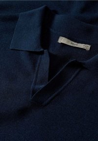 Polo en maille marine avec col à revers, texture douce et étiquette présentant les informations de la marque, mettant en avant un design minimaliste.