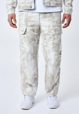 Lichtgekleurde cargobroek met een gestructureerd, abstract patroon, voorzien van meerdere zakken en een relaxte pasvorm, gecombineerd met witte sneakers.