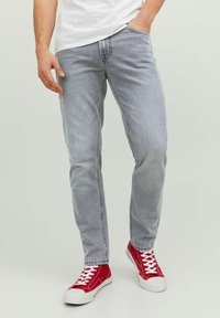 Jean en denim gris clair avec une coupe droite, présentant des poches avant et une couture minimale, associés à des baskets montantes rouges.