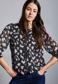 Černá a šedá blůza se vzorem, vyrobená z texturované, průsvitné látky a se třičtvrtinovými rukávy. Zapínání na knoflíky vpředu a volný střih.