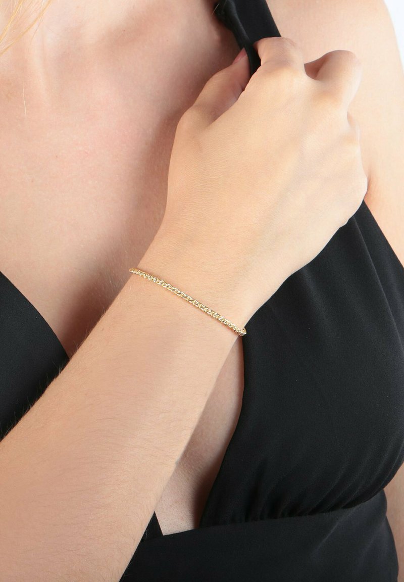 Goldene Kettenarmband, getragen am Handgelenk, mit einem filigranen Design aus verbundenen Mustern und einer glatten, glänzenden Oberfläche.