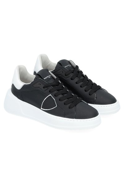 Black leather sneakers with white rubber soles; featuring a low-top design, rounded toe, and black laces. Accented with a white heel.