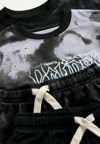 Két rövid ujjú felső fekete és szürke batikolt mintával, bordás nyakkivágással, valamint egy pár fekete, gumis derekú és zsinórral ellátott sort.