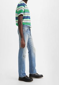 Camisa de manga corta a rayas en verde, azul y blanco; combinada con vaqueros desgastados azul claro; zapatos negros lisos con cordones.