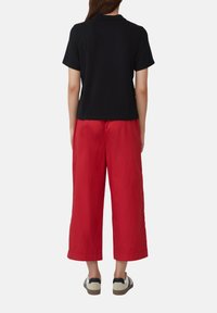 T-shirt noir à manches courtes associé à un pantalon rouge ample. Le t-shirt a une coupe droite ; le pantalon est en tissu léger avec une coupe décontractée.