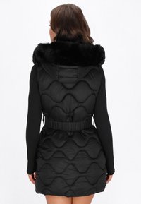 Czarna kamizelka puchowa z odpinanym kołnierzem z sztucznego futra, elastycznym paskiem w talii i pikowanym wzorem, widziana z tyłu. Gładka tekstura.