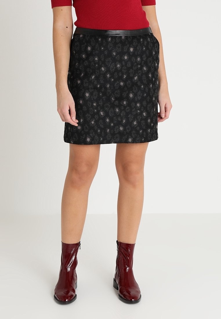 Falda negra texturizada con un sutil patrón floral, que cuenta con una cintura ajustada y una banda en la cintura de aspecto suave y similar al cuero. Se lleva con botas cortas burdeos brillantes.