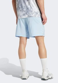 Svetlomodré športové šortky s hladkou textúrou, mierne voľným strihom a bočnými rozparokmi; nosené s bielymi teniskami a ponožkami.