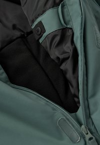 Groene buitenjas met een fleece voering, zwarte binnenstof, een ritssluiting en een knopriem. Geweven materialen doorheen.